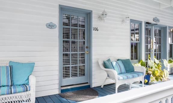 A porch off a bed and breakfast guest room, featuring blue trim and decor against white walls and furnishings