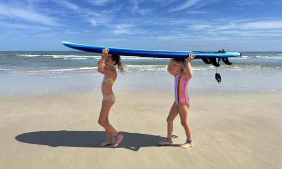 Two girls carrying a surfboard on the beach