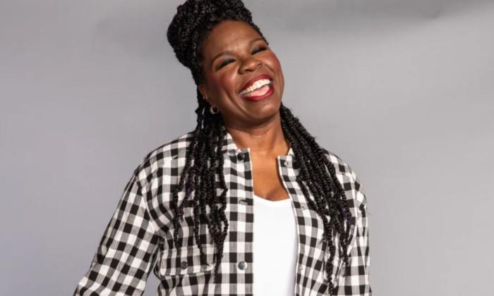 Comedian Leslie Jones smiles in front of a grey backdrop.