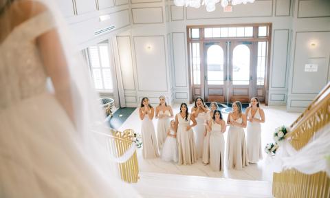 The bridal attendants gazing up at the bride who is standing at the top of the stairs