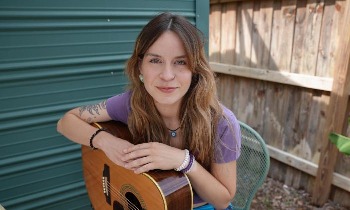 Riggy, singer and songwriter, sitting outside with her guitar