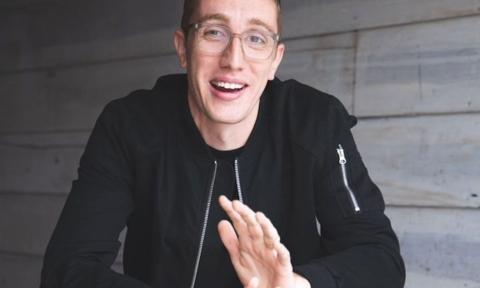 Sam Salem wears glasses and smiles in front of a grey backdrop. 