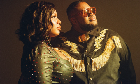 Bandmates from The War and Treaty wear black clothing and pose in front of a dark brown backdrop.