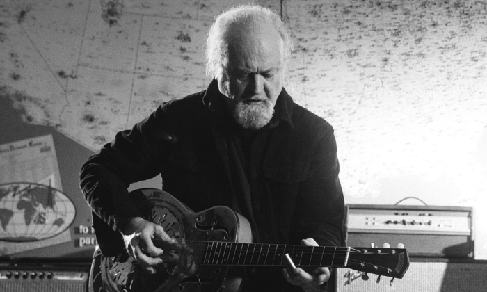 Tinsley Ellis plays his guitar against a backdrop featuring a world map.